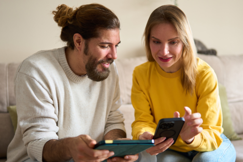 Casal a comparar informação num tablet e telemóvel, sentados no sofá