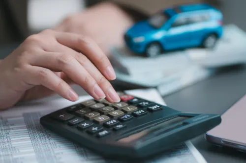 Pessoa a usar calculadora com carro em miniatura e documentos ao fundo