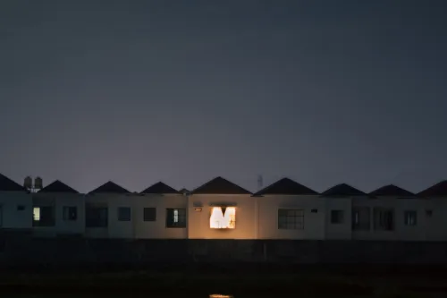 Fila de casas ao anoitecer, com uma janela iluminada a destacar-se